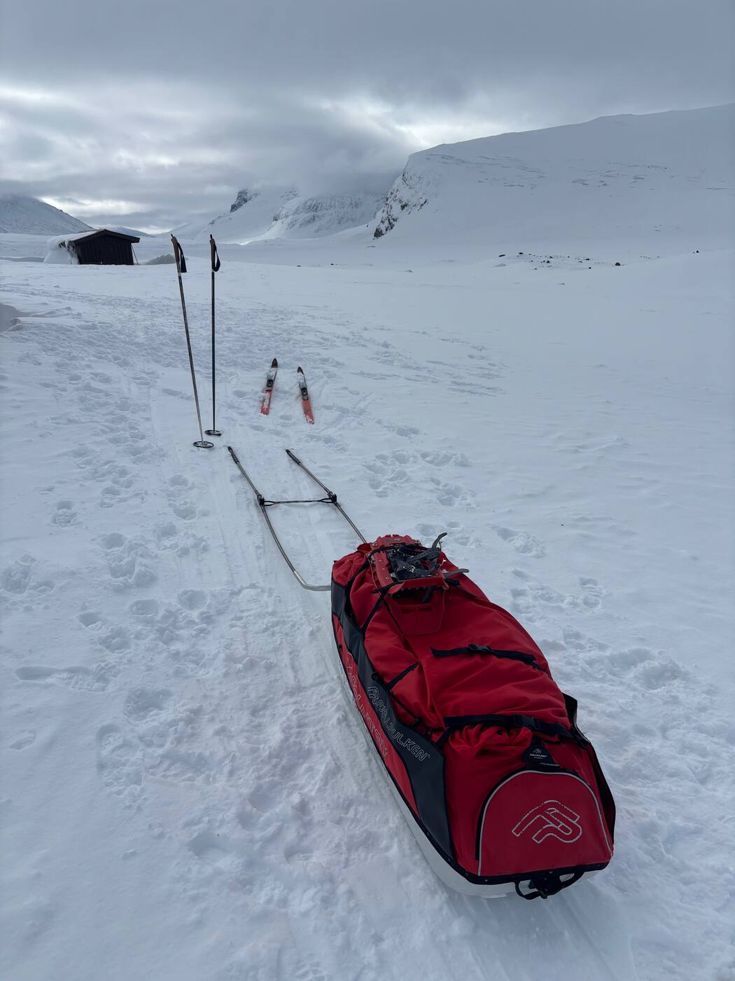 Pulka Fjellpulken rouge devant une cabane et un cirque